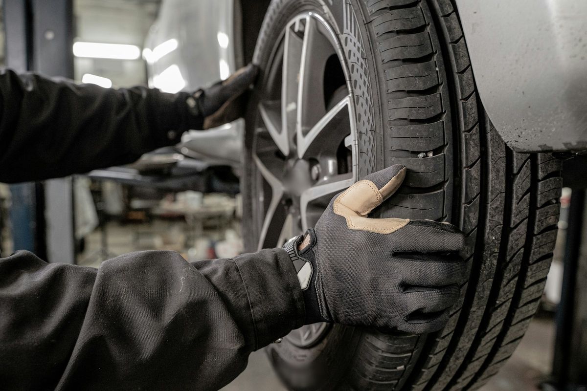 Handen in werkhandschoenen zetten een wiel op een wagen in de werkplaats